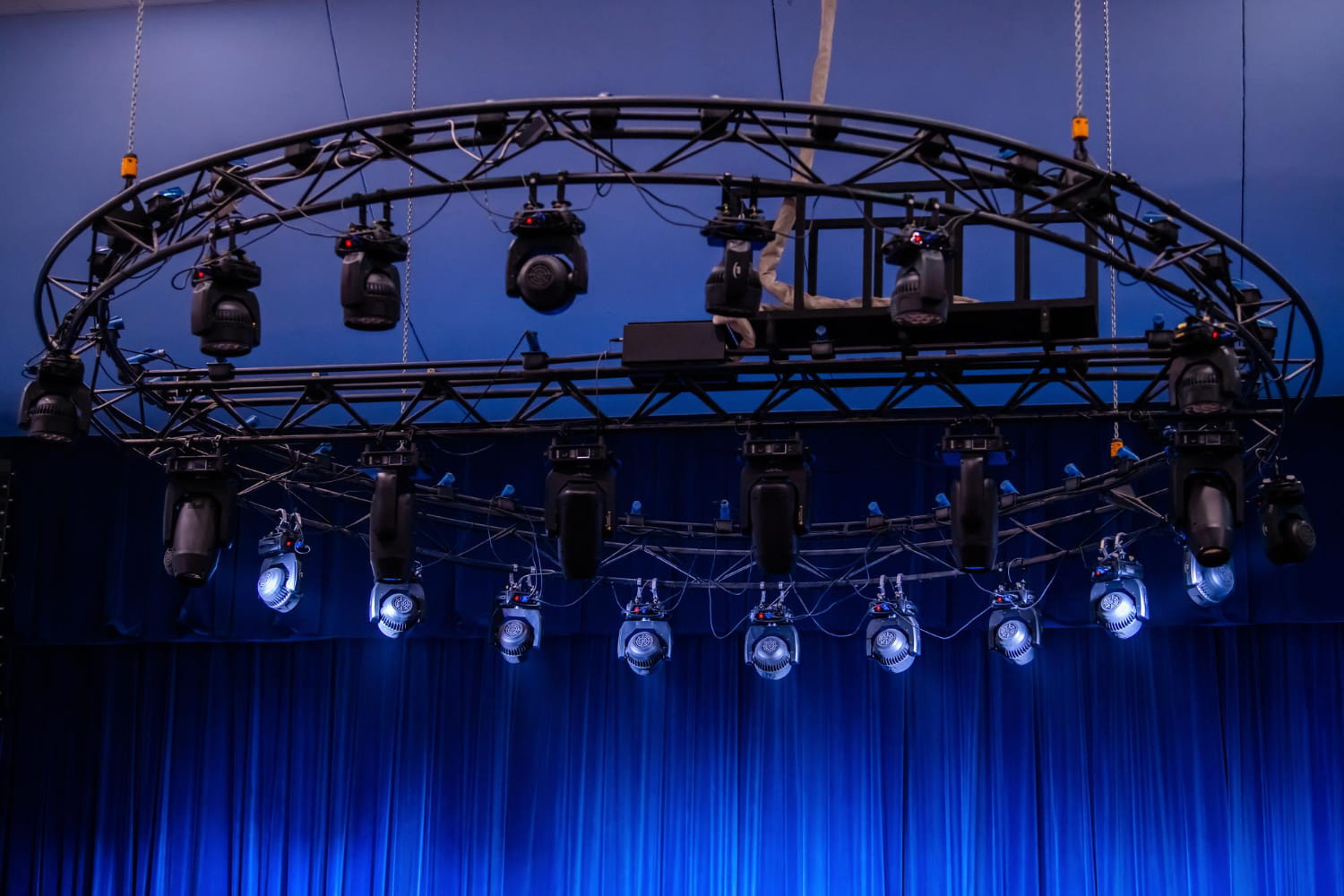 Circular truss of stage lights suspended above a blue curtain stage.