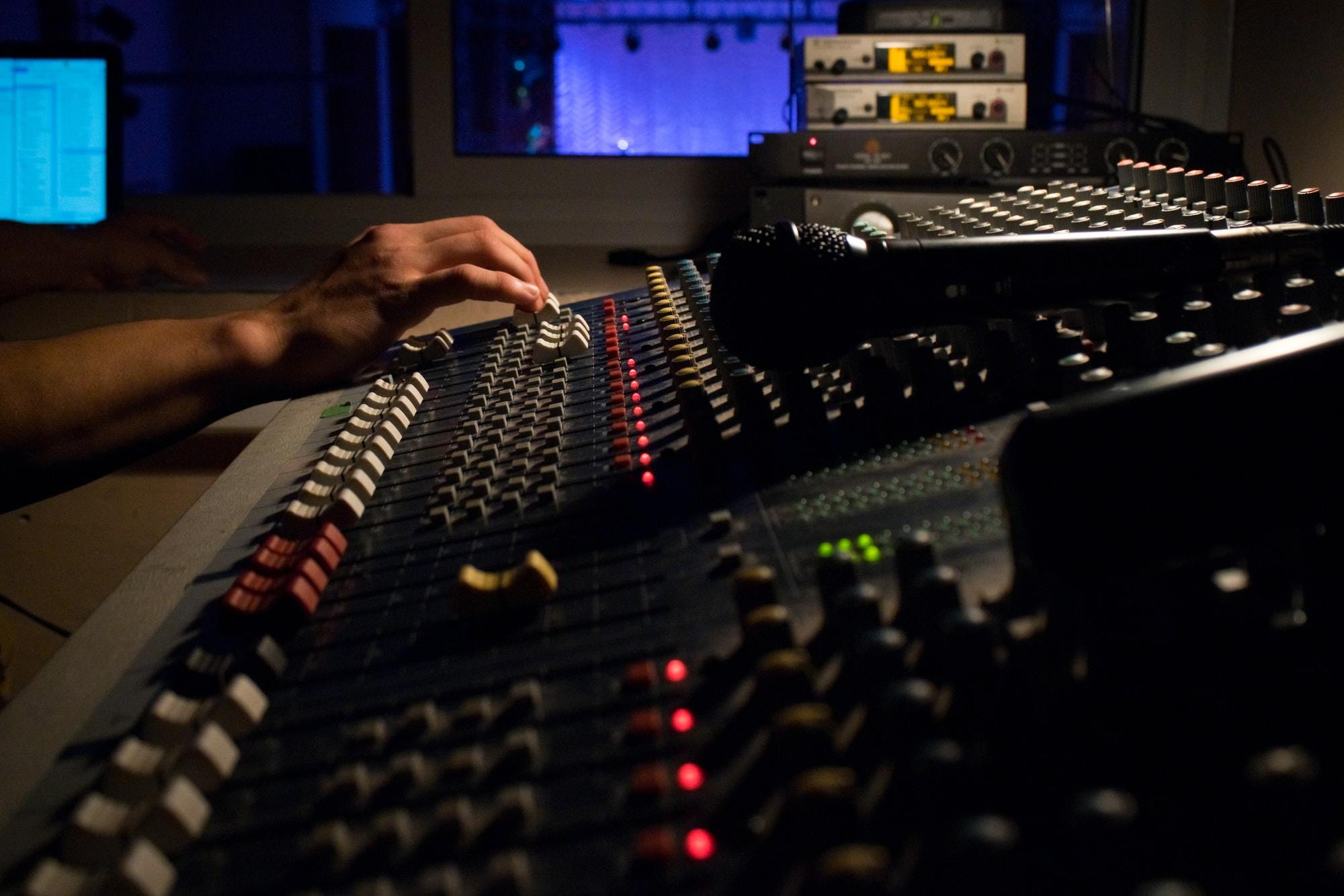 Close-up of a sound engineer's hand adjusting knobs on a large mixing console in a dimly lit recording studio.